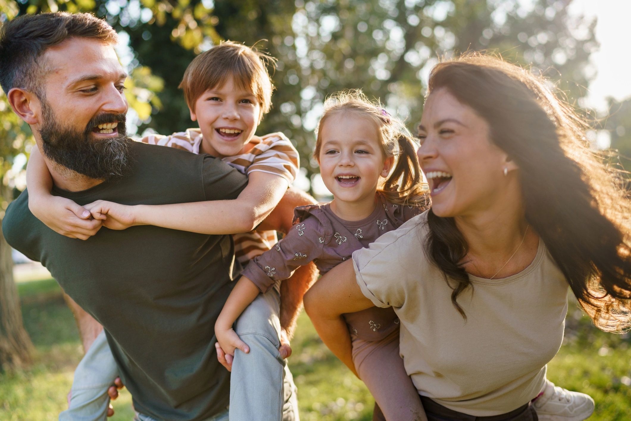 Family enjoying piggyback rides outdoors laughing together
